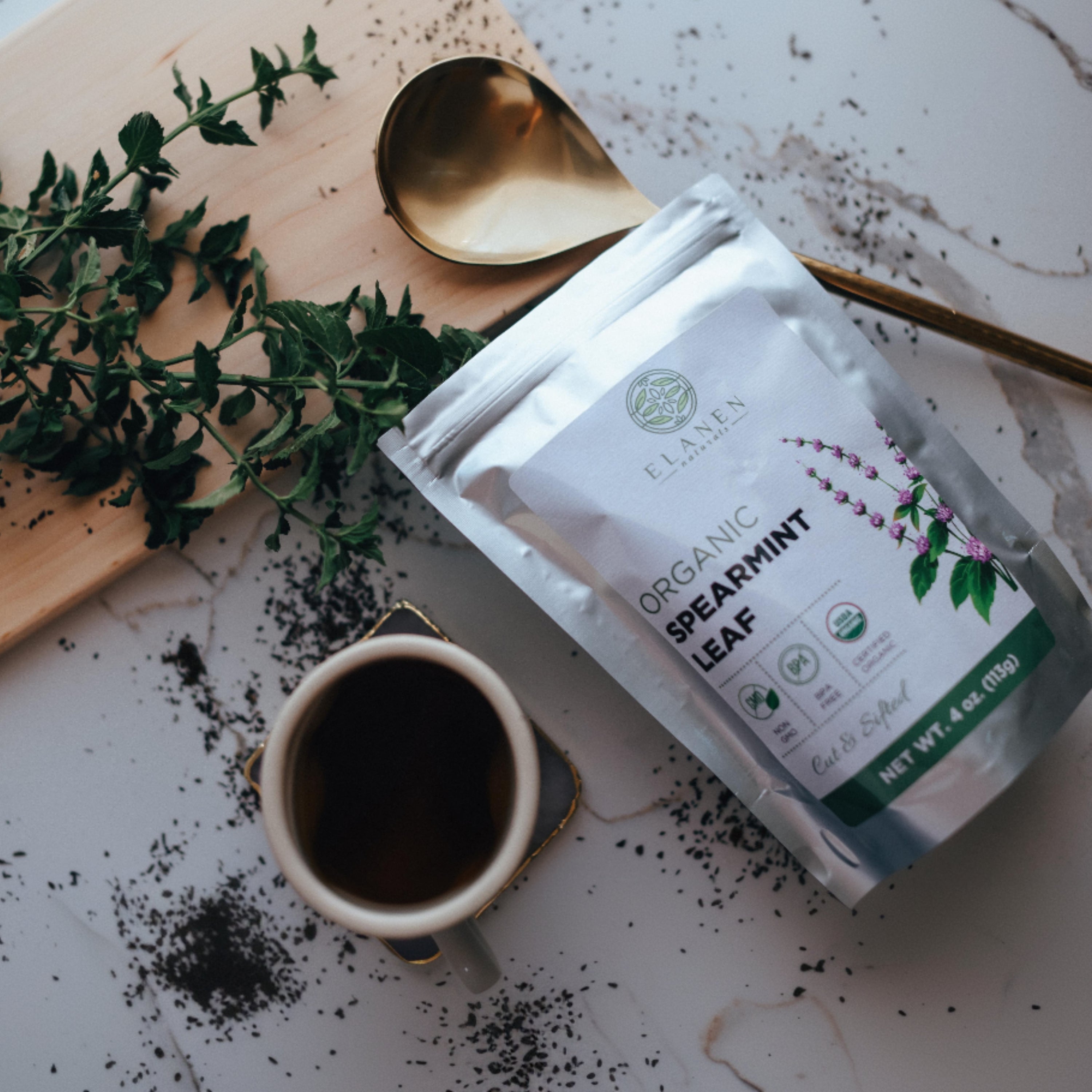 Package of Organic Spearmint Leaf on a table with a cup of coffee and mint leaves.