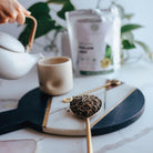 Tea-making setup with a teapot, cup, and spoonful of mullein leaves on a marble surface.