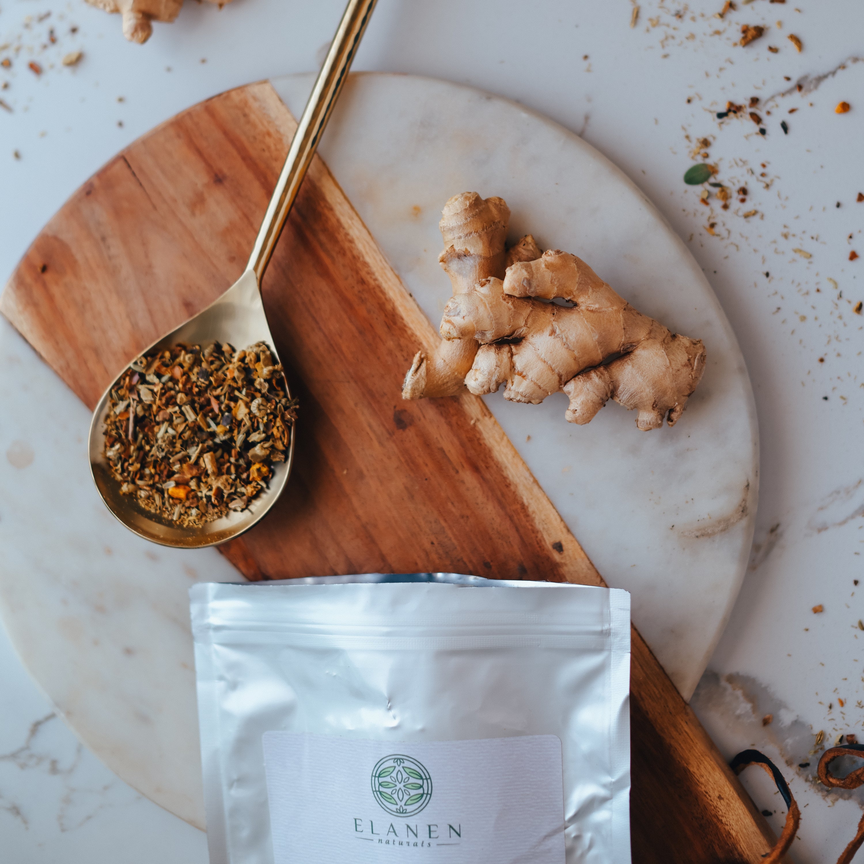 Ginger root, dried herbs, and a package of Elanen on a marble surface.