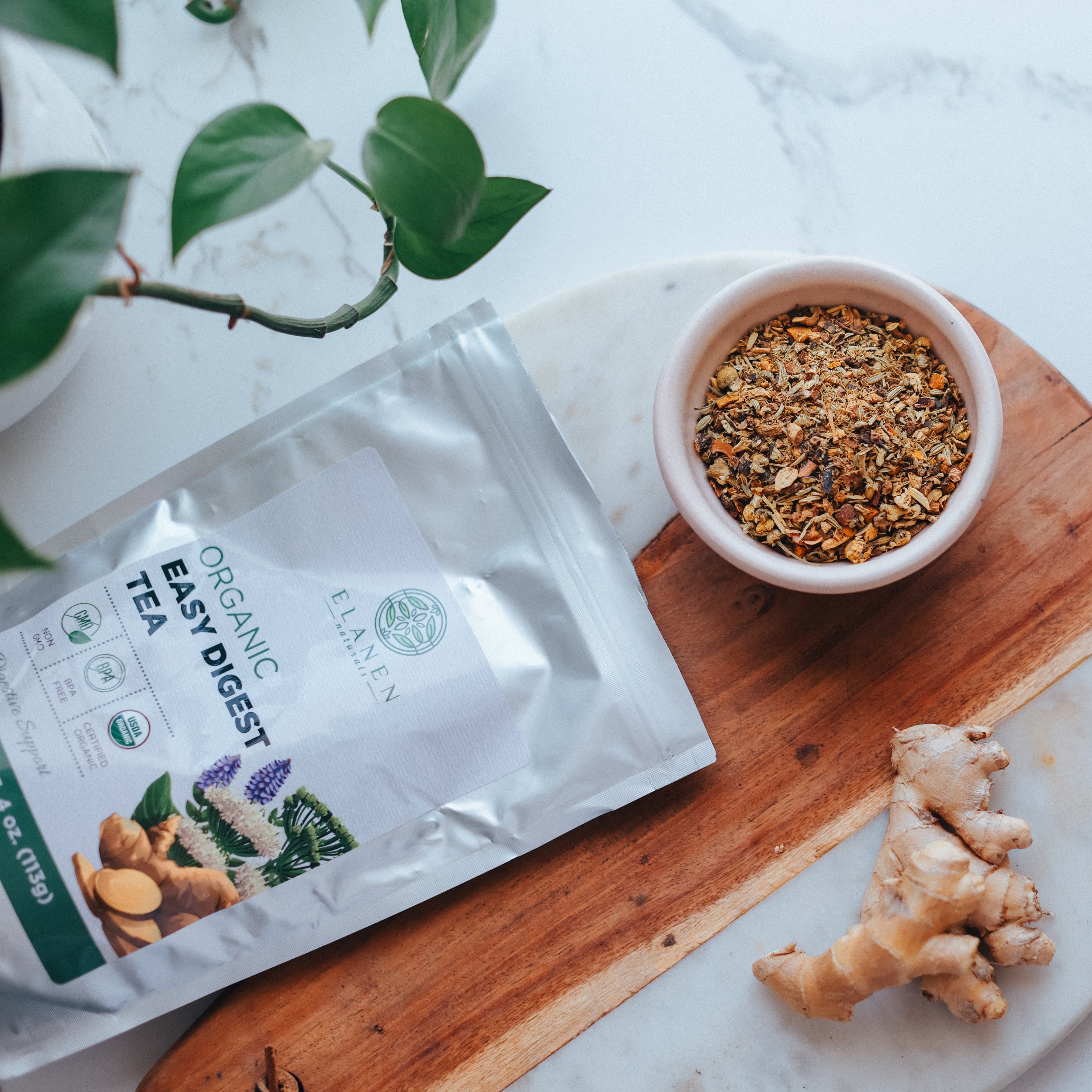 Tea package labeled 'Easy Digest' on a wooden board with a bowl of tea leaves and ginger root.