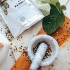Mortar and pestle with dried herbs on a wooden board, and green leaves.