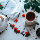 Tea cup with teapot, tea leaves, and raspberries on a marble surface