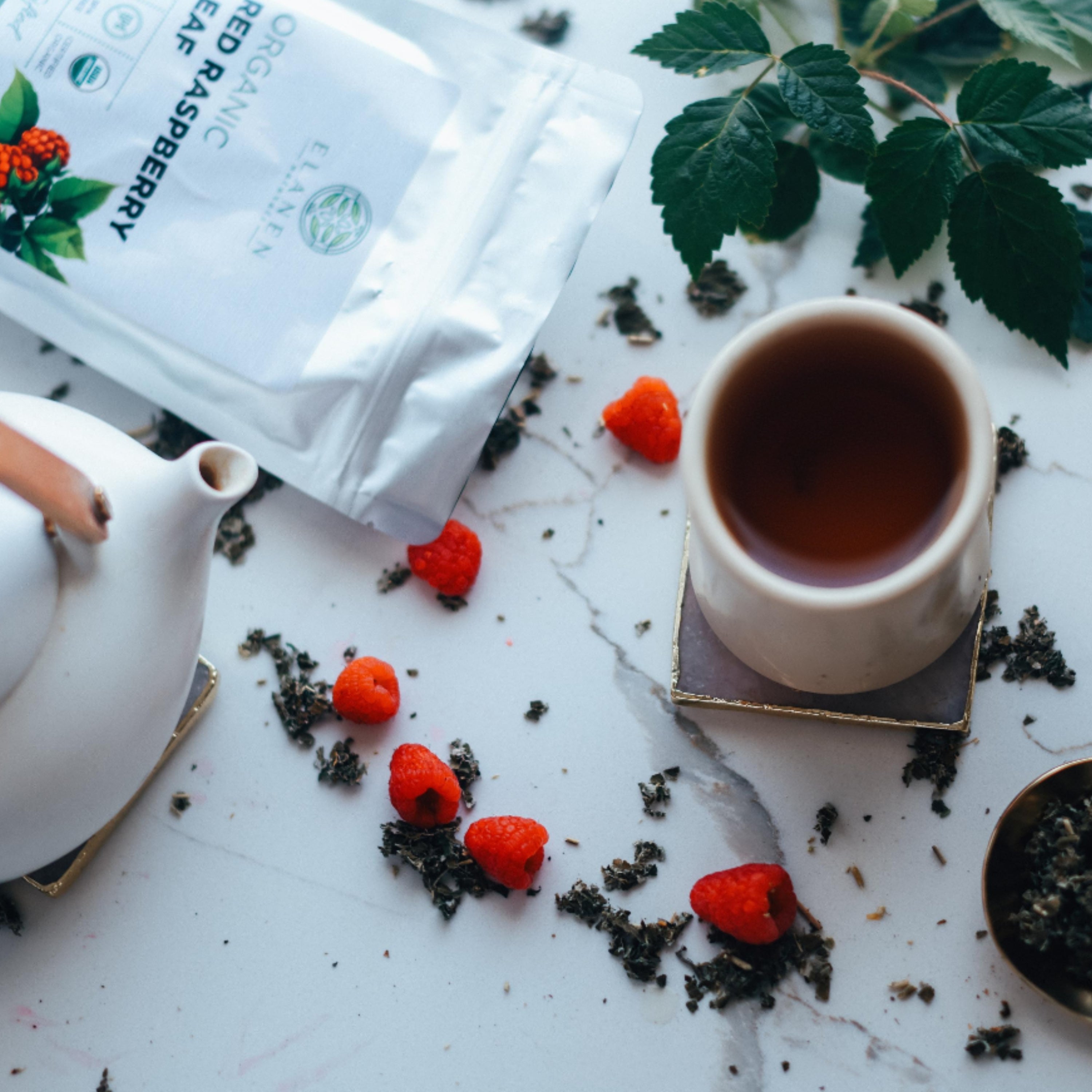 Tea cup with teapot, tea leaves, and raspberries on a marble surface