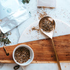 Gold spoon and bowl with dried herbs on a wooden board