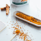 Turmeric powder on a wooden spoon and dish with turmeric root and container in the background.