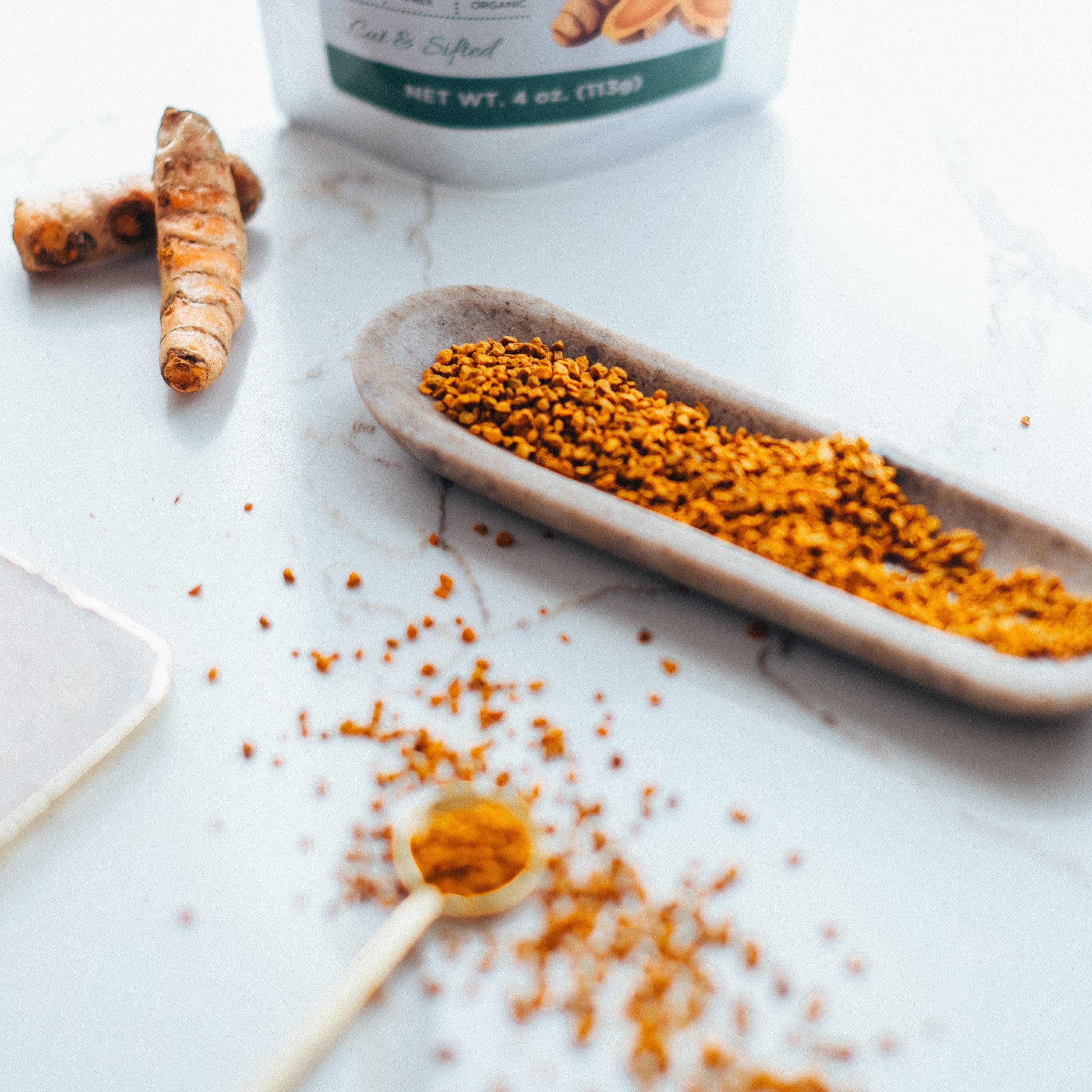 Turmeric powder on a wooden spoon and dish with turmeric root and container in the background.