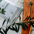 Olive leaf product packaging on a marble surface with olive branches.