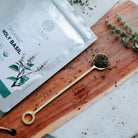 Elaven Organic Holy Basil packaging on a wooden board with a spoonful of herbs.