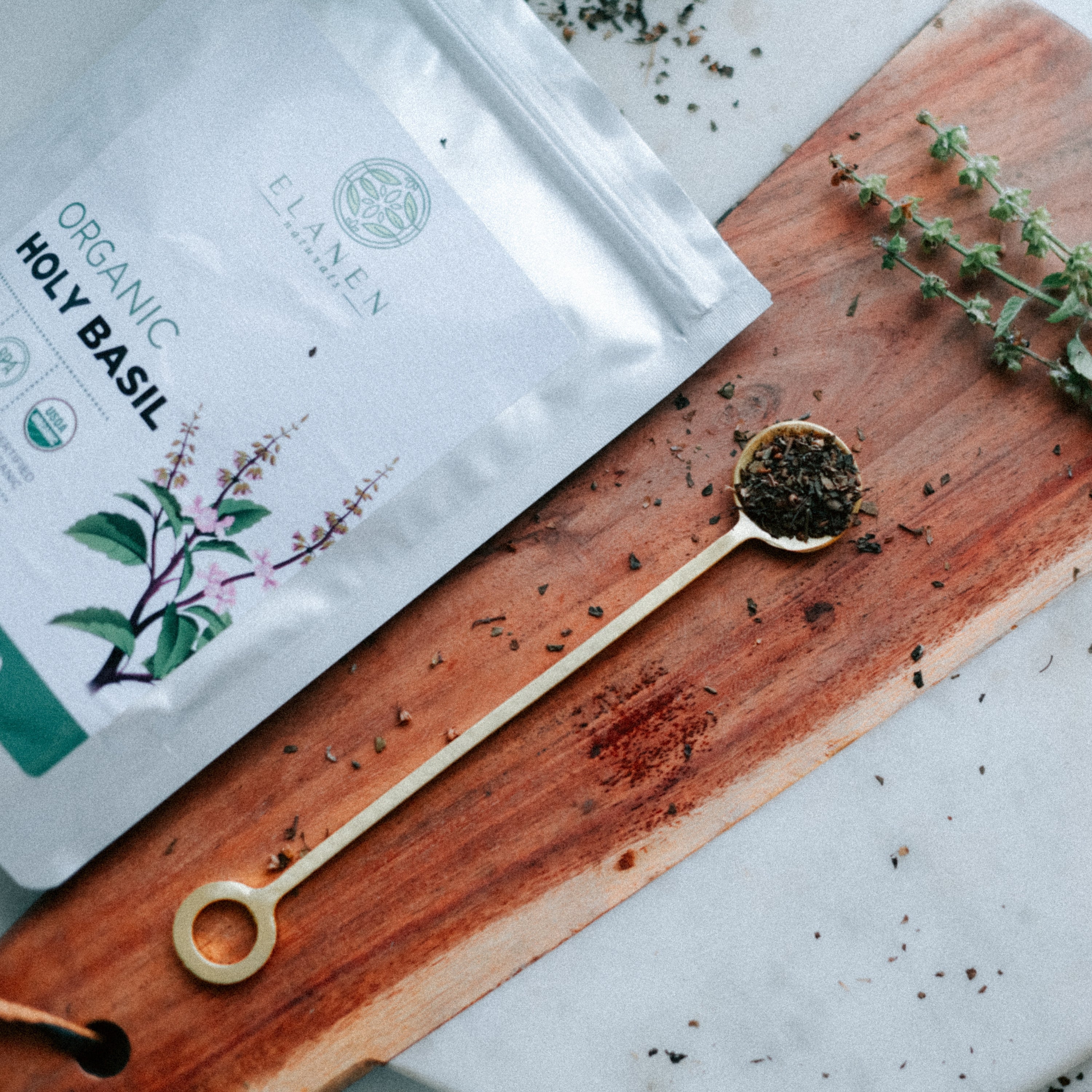 Elaven Organic Holy Basil packaging on a wooden board with a spoonful of herbs.