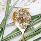 Gold spoon filled with dried lemongrass on a white background with green leaves.