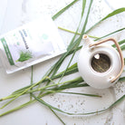 White teapot with dried lemongrass and a package of lemongrass on a white surface