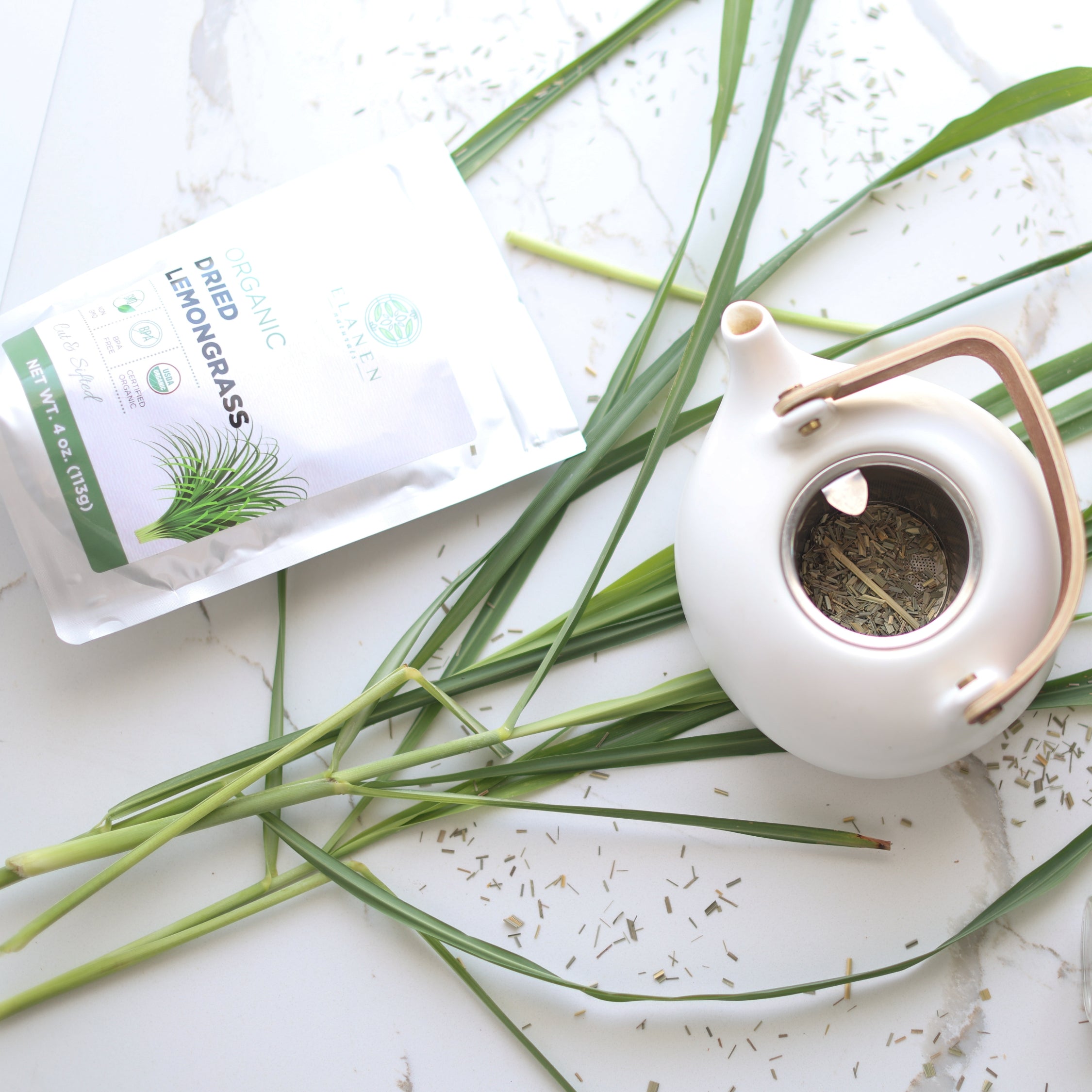 White teapot with dried lemongrass and a package of lemongrass on a white surface