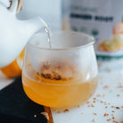 Ginger tea being poured into a glass with a lemon in the background.