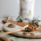 Clear jar with dried wormwood on a wooden spoon and plate, blurred background