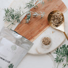 wormwood leaves on a wooden board with a marble surface, featuring a gold spoon and packaging.
