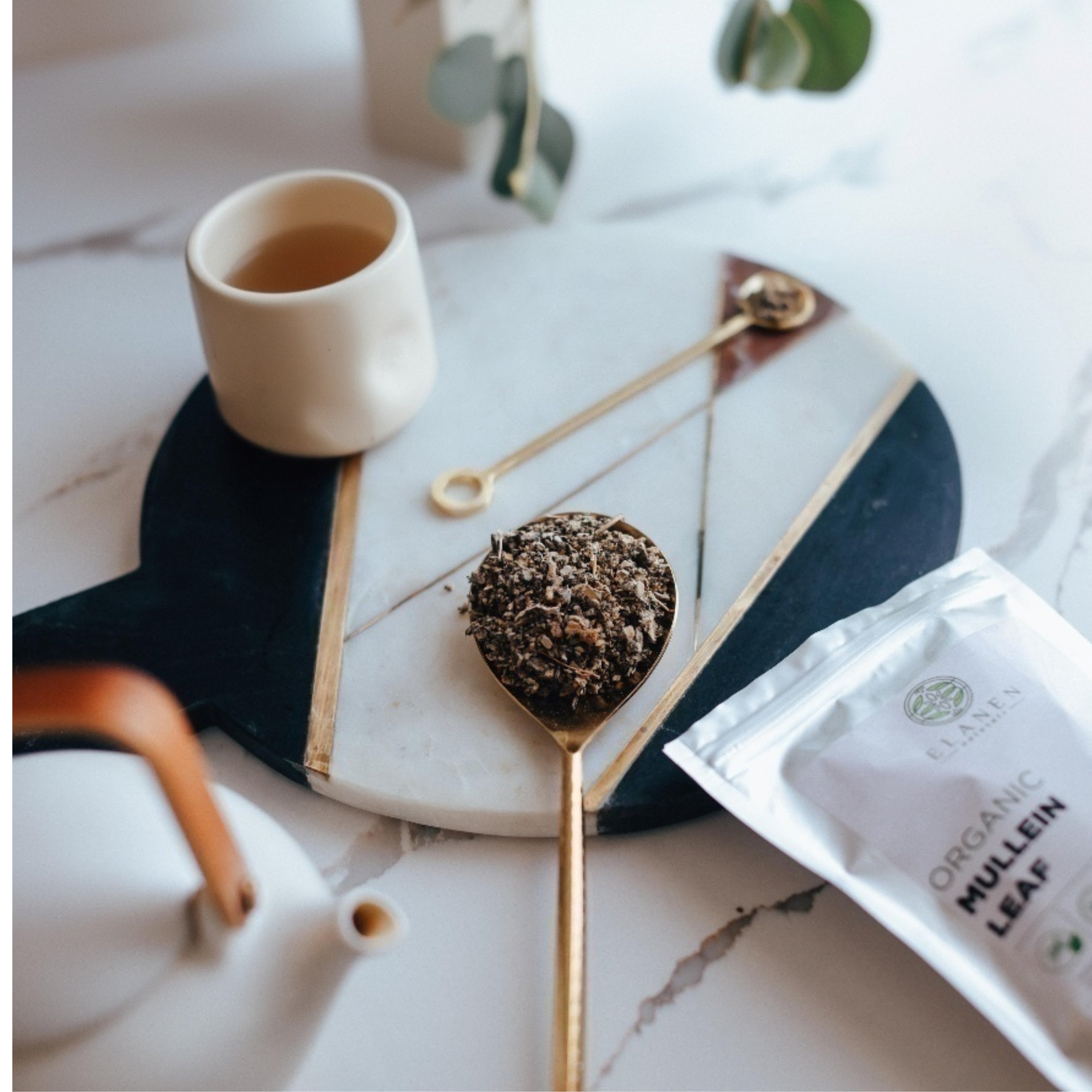 Tea cup, spoon with mullein leaves, and organic mullein leaf packaging on a marble surface