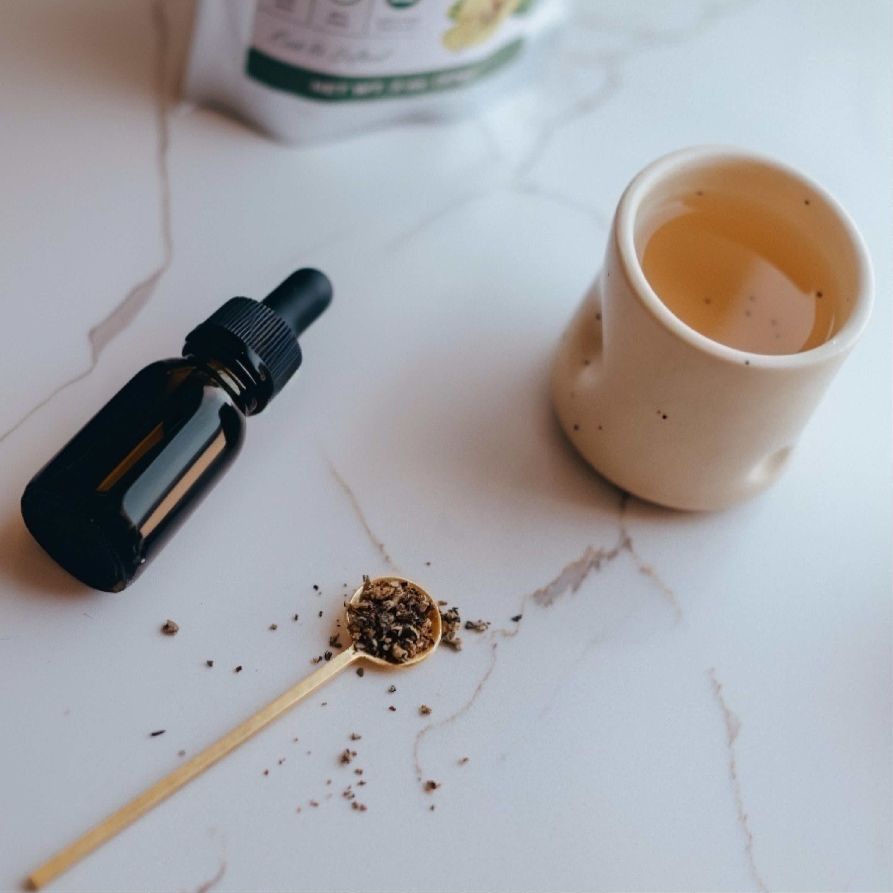 Tea cup, dropper bottle, and spoon with mullein leaves on a marble surface