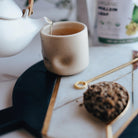 Tea being poured from a white teapot into a ceramic cup on a marble surface.