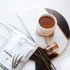 Tea packaging with a cup of tea, a bottle, and herbs on a white surface
