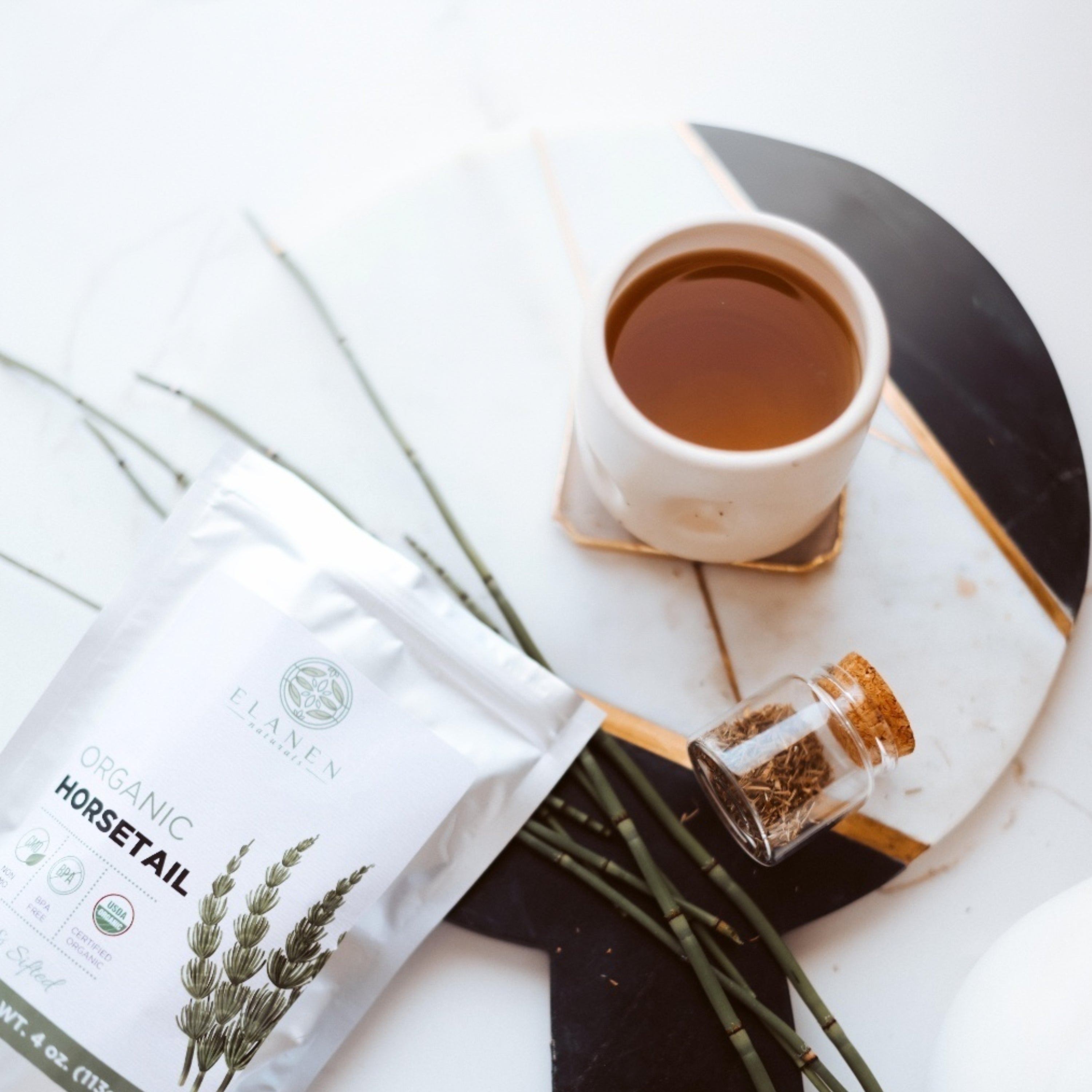 Tea packaging with a cup of tea, a bottle, and herbs on a white surface
